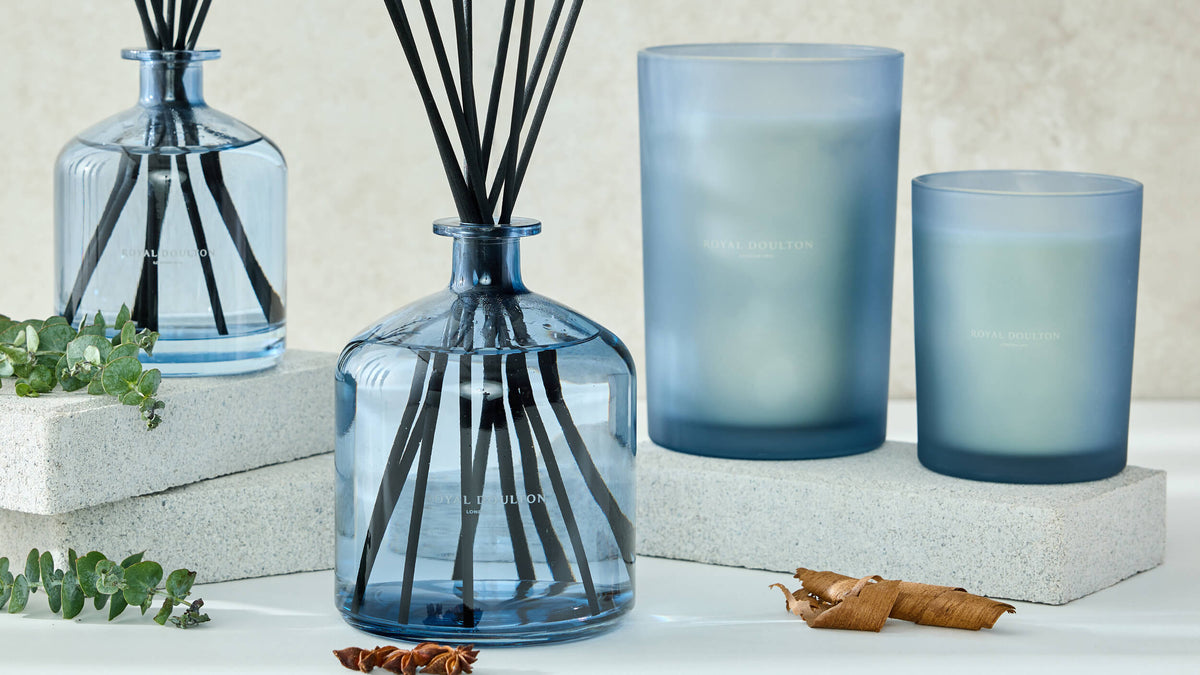 Montclair blue glass reed diffusers and two blue candle vessels arranged on pale blocks with foliage