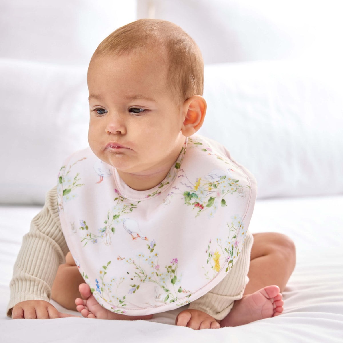 Seated baby wearing a pale pink Twill & Co bib with flowers, geese and rabbit illustrations