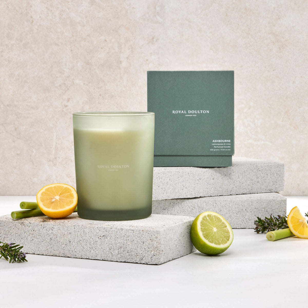 Royal Doulton Ashbourne 500g candle in a green vessel beside its packaging box, with lemon and lime on pale blocks.