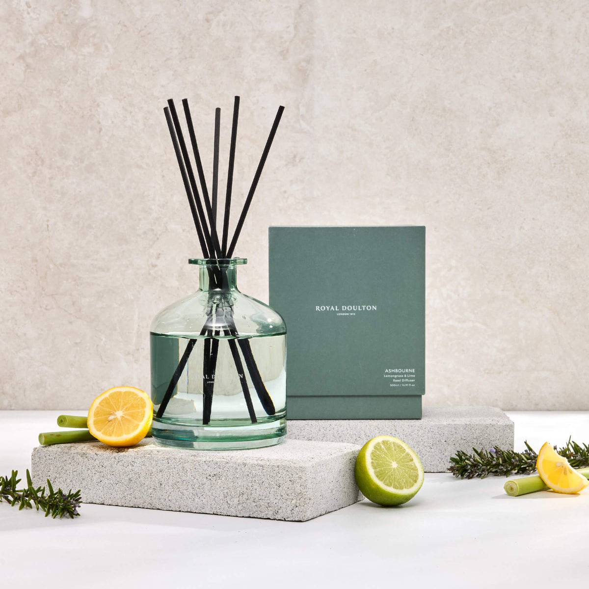Royal Doulton Ashbourne 500ml diffuser with black reeds in a green glass bottle, beside its box and citrus fruit.