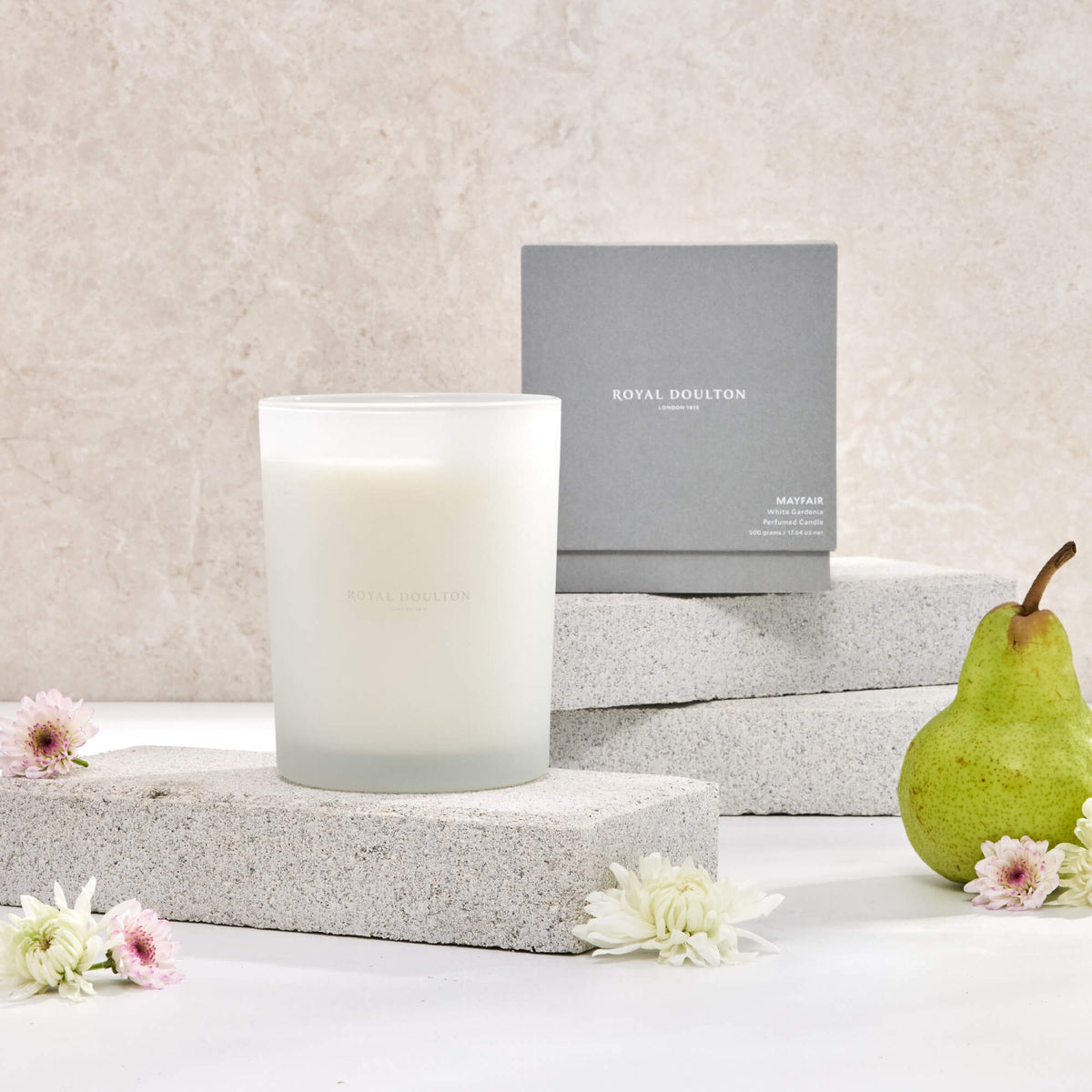 Royal Doulton Mayfair 500g candle in a white vessel with a grey packaging box, styled with a pear and flowers.