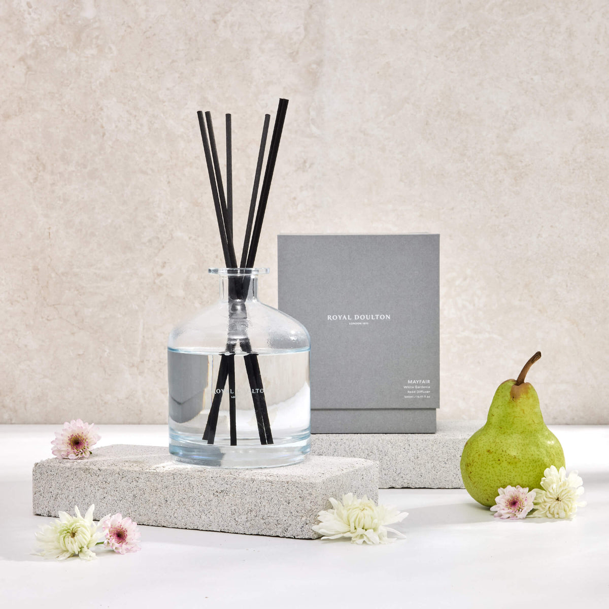 Royal Doulton Mayfair 500ml diffuser with black reeds in a clear glass bottle, beside its grey box, pear and flowers.