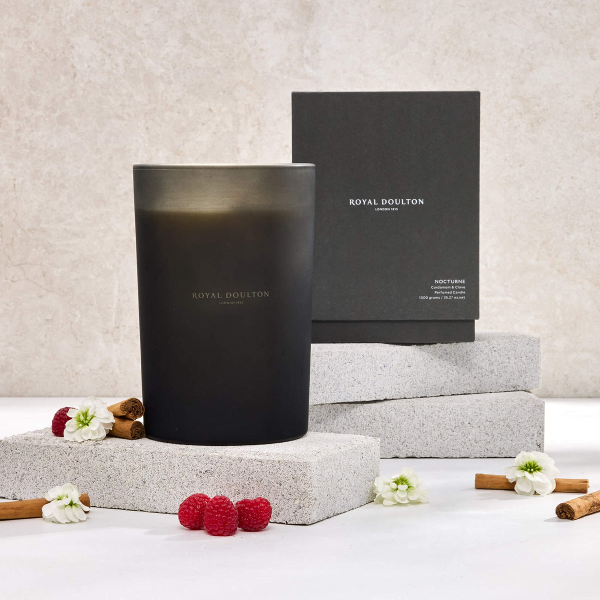 Royal Doulton Nocturne 1000g candle in a tall dark vessel with its black box, raspberries and white flowers on pale blocks.