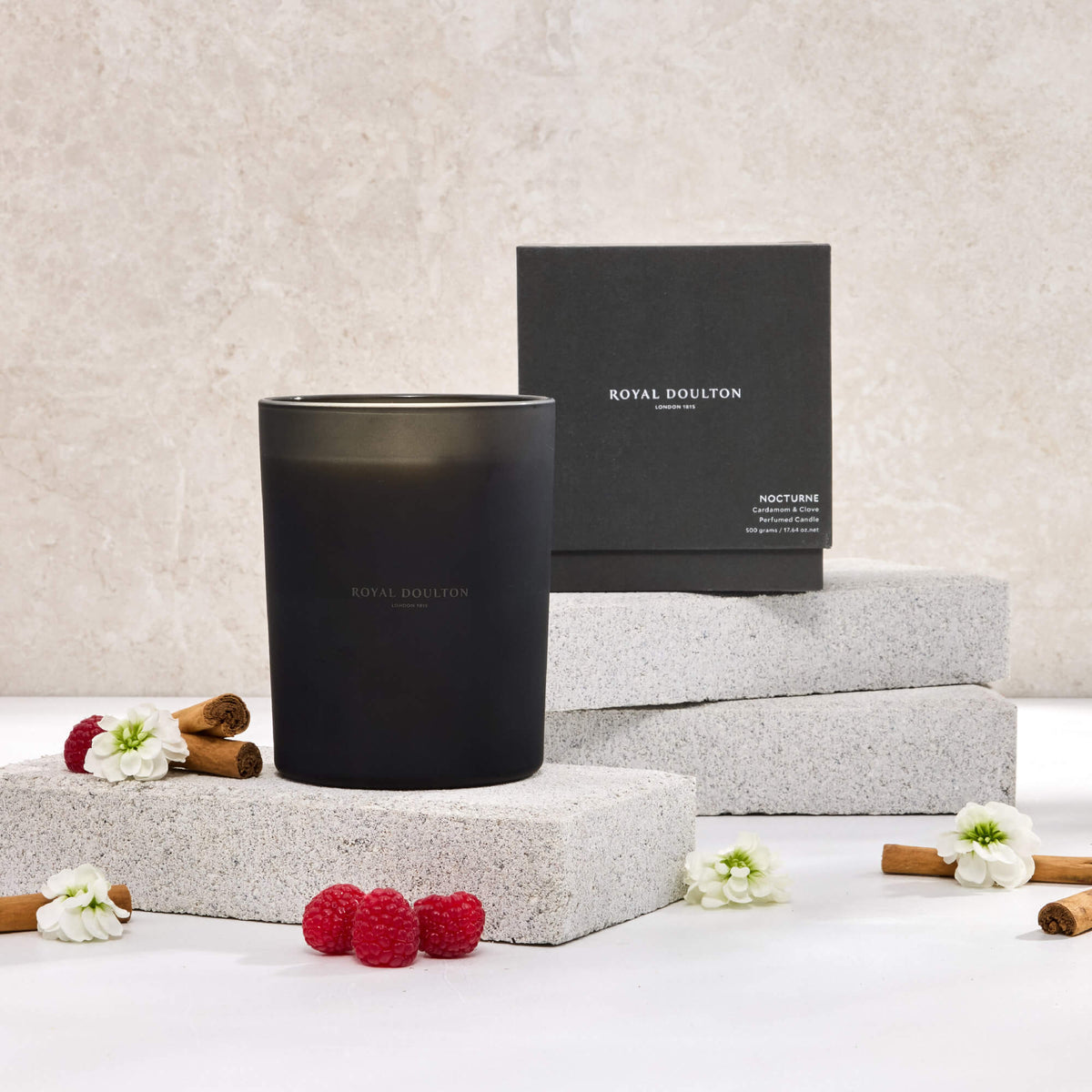 Royal Doulton Nocturne 500g candle in a dark vessel beside its black packaging box, with raspberries and white flowers.