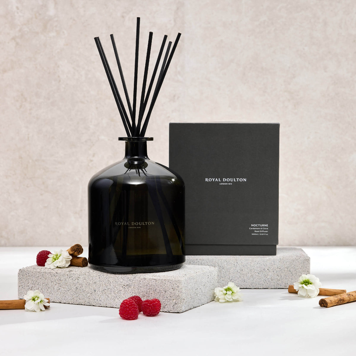 Royal Doulton Nocturne 1000ml diffuser and black packaging box on pale blocks, with black reeds, raspberries and white flowers.