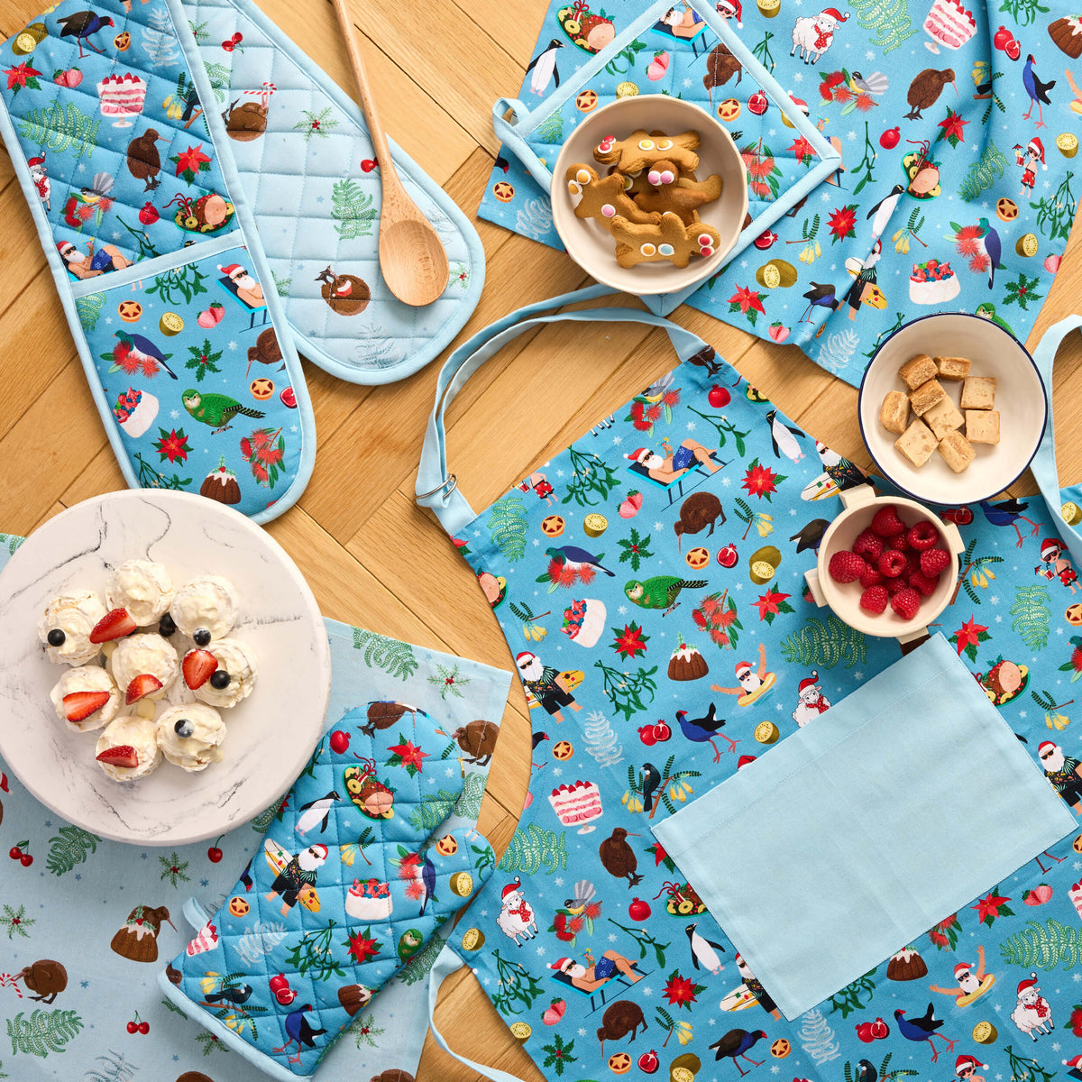Blue Twill & Co Kiwiana Christmas apron, quilted oven gloves and tea towels arranged with baking ingredients