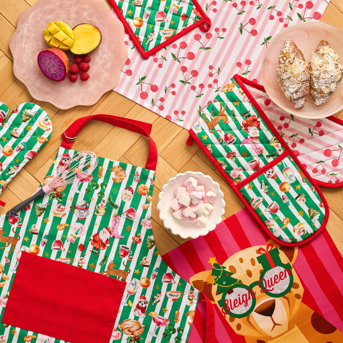 Green-striped Twill & Co Christmas apron and oven gloves with cherry and Sleigh Queen tea towels
