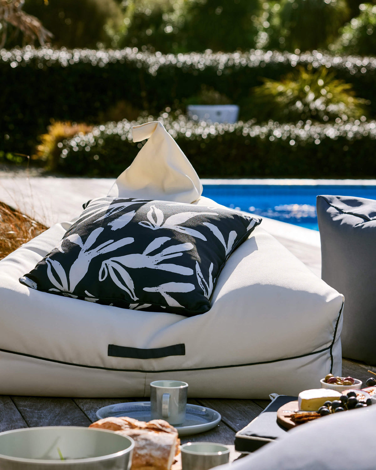 Cream Twill & Co outdoor bean bag with a black botanical cushion beside a swimming pool