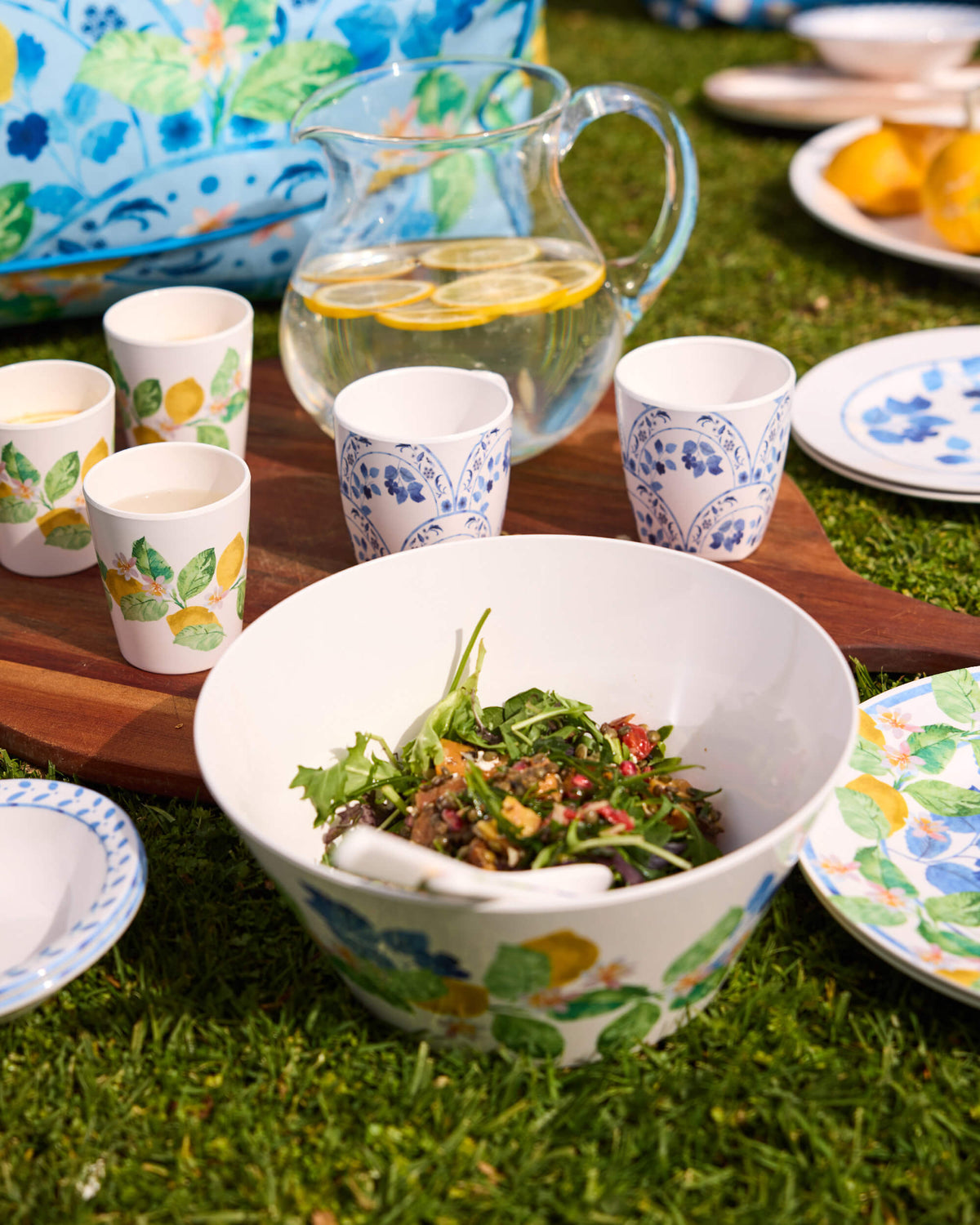 Floral Twill & Co salad bowl beside patterned cups and a lemon-water jug on a garden picnic setting
