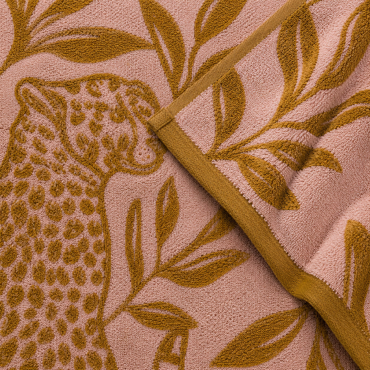 Close-up of an ochre leopard, foliage and folded border on a pink Twill & Co Wild Thing towel