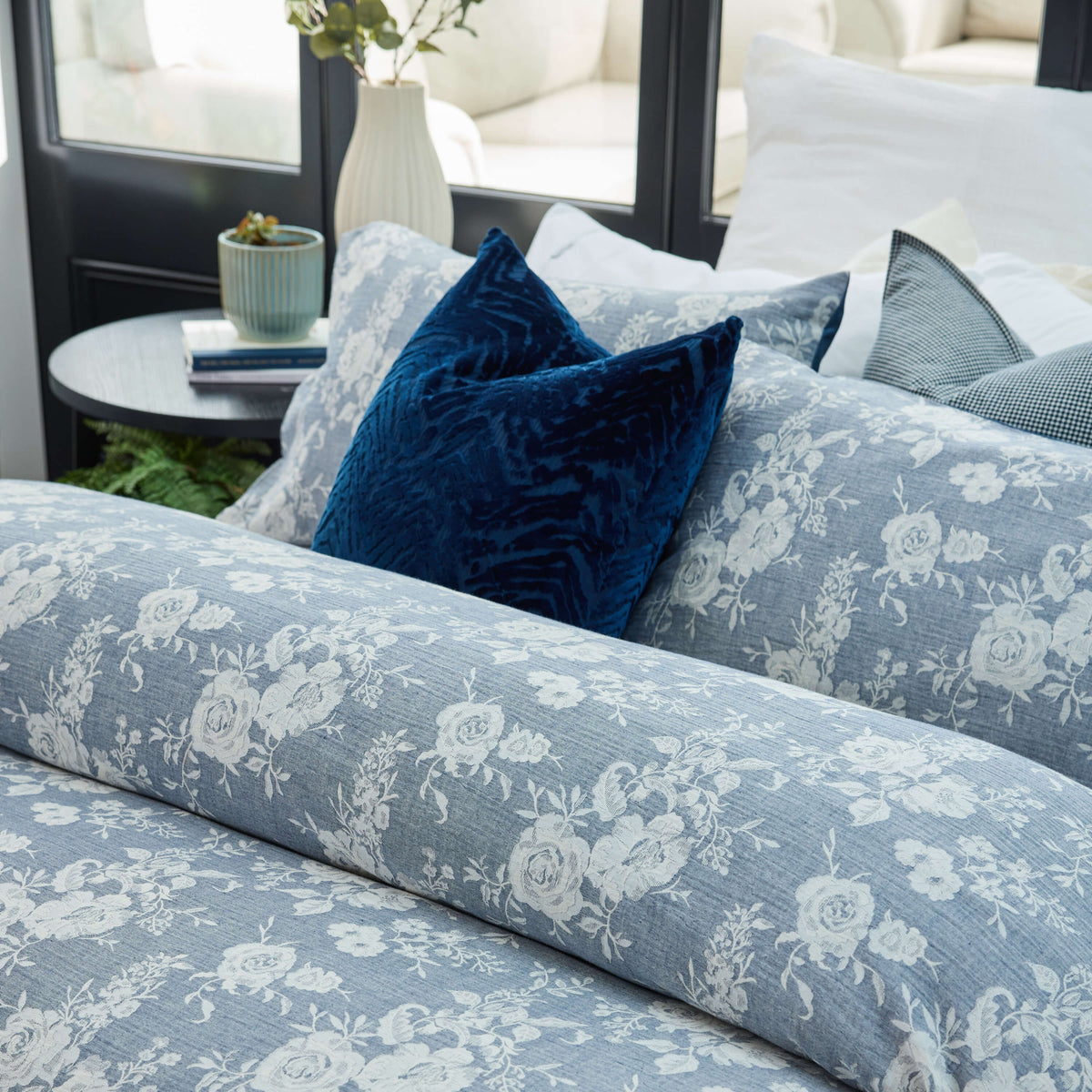 June & Jupiter blue-grey floral bedding with dark blue cushions beside a window