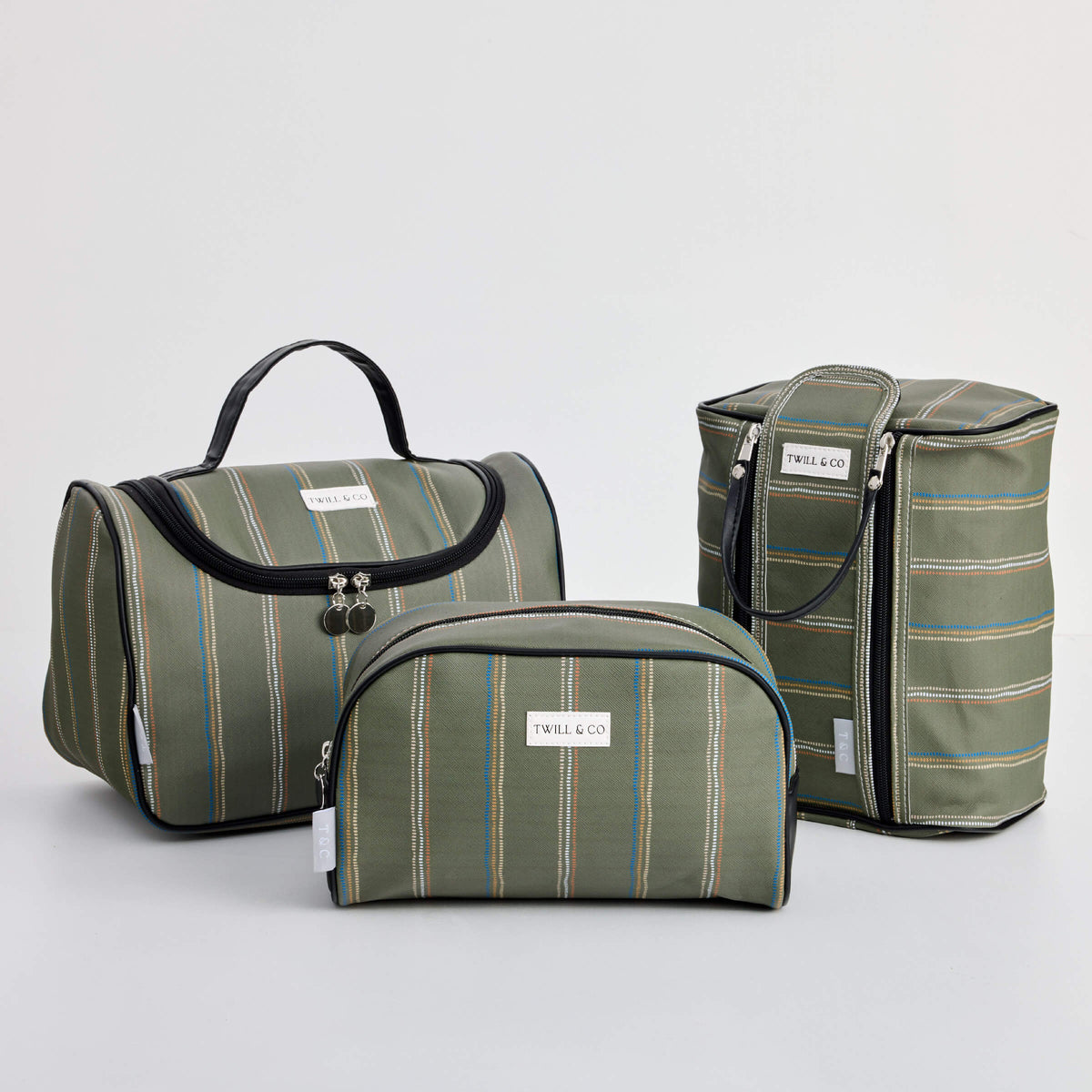 Three olive-striped Twill & Co Beau toiletry bags in different shapes with dark handles and trim