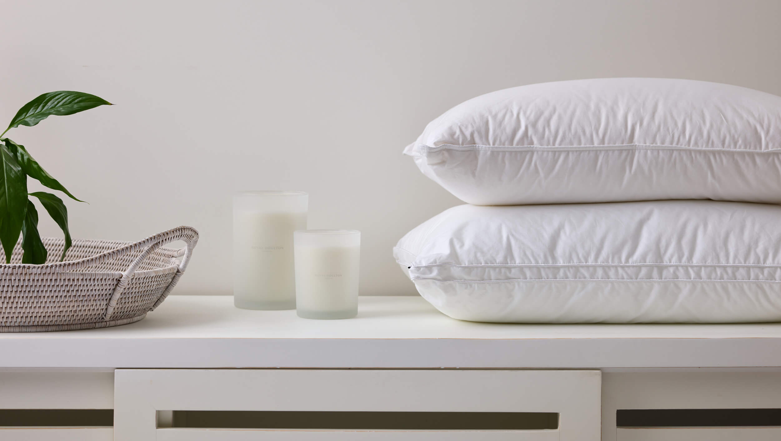 Royal Doulton white pillow inners stacked on a cabinet with candles and a plant