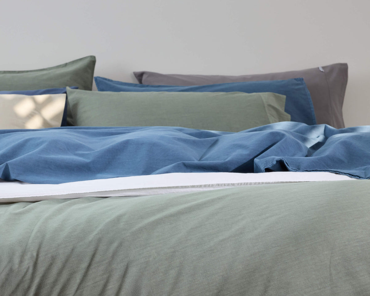 Royal Doulton Nelson blue, sage and charcoal sheets layered on a bed
