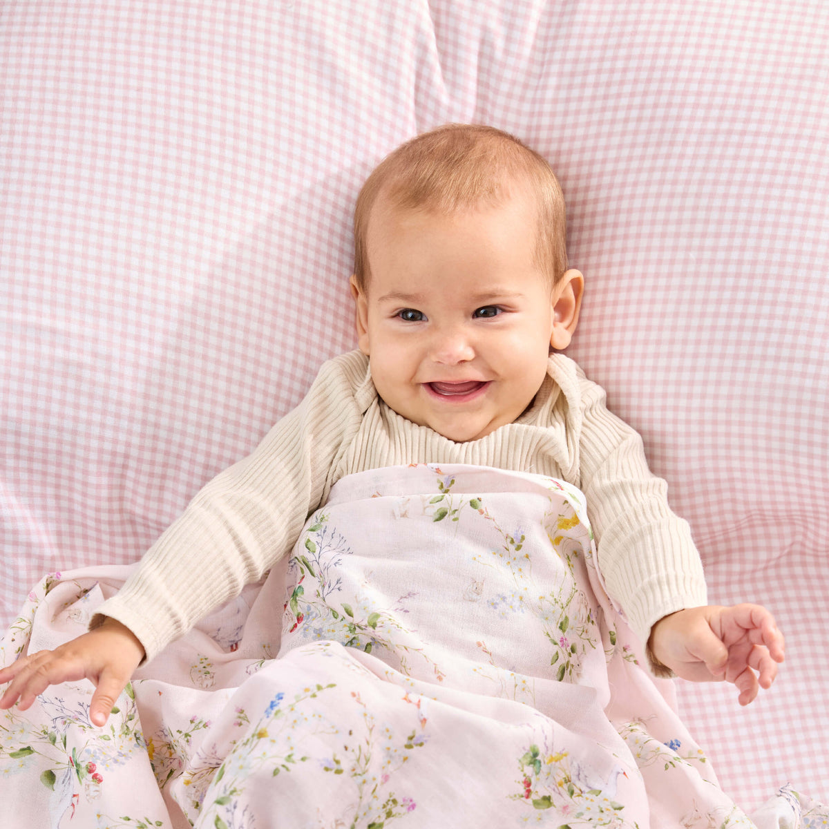 Baby with a pale pink floral Twill & Co wrap, resting on pink gingham bedding