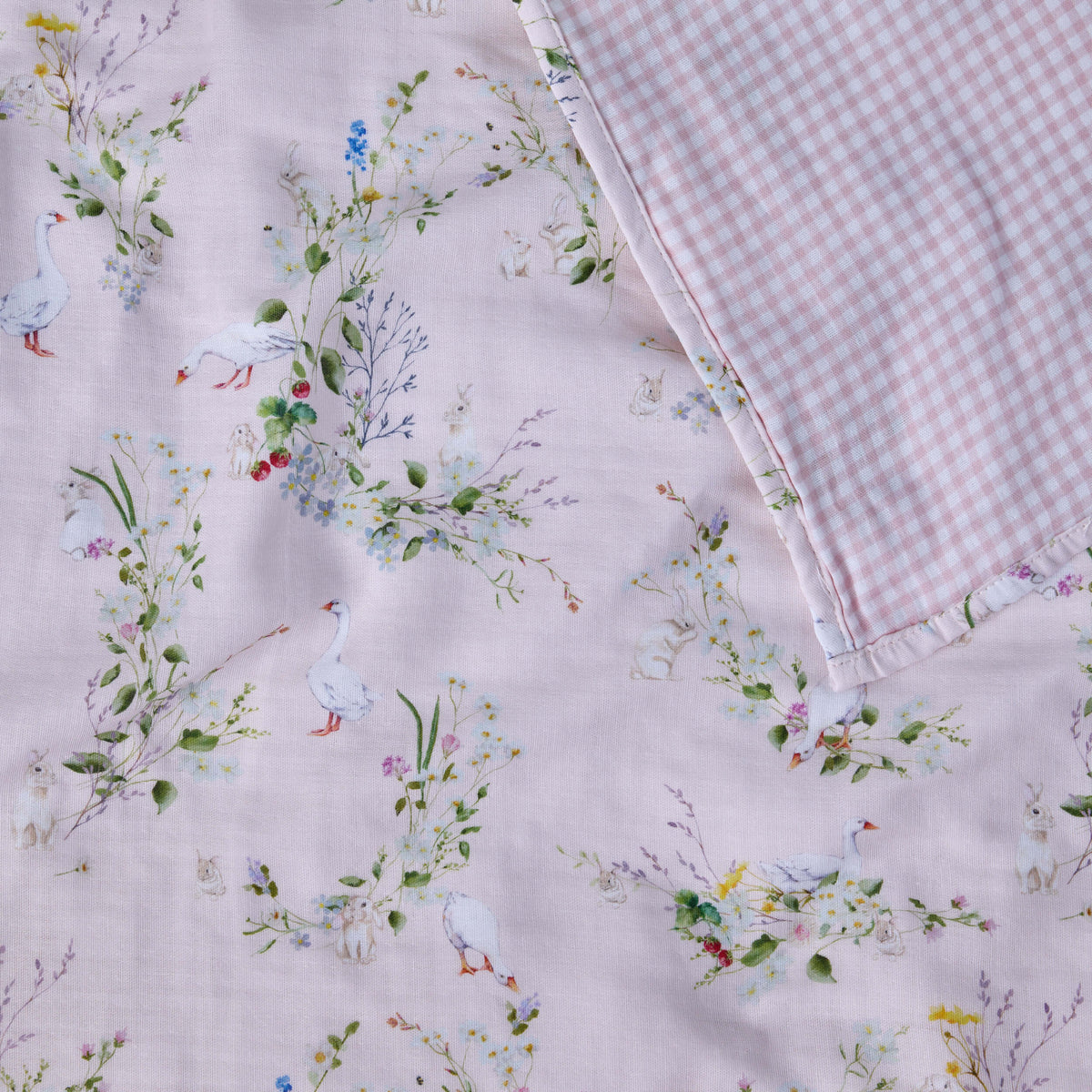 Close-up of Twill & Co pink nursery fabric with flowers, white geese and rabbits beside pink gingham