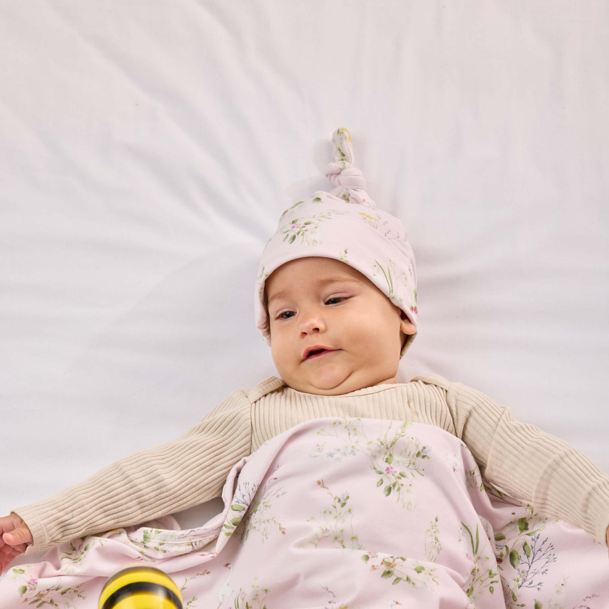 Baby wearing a pink floral Twill & Co knotted hat with a matching wrap across their lap