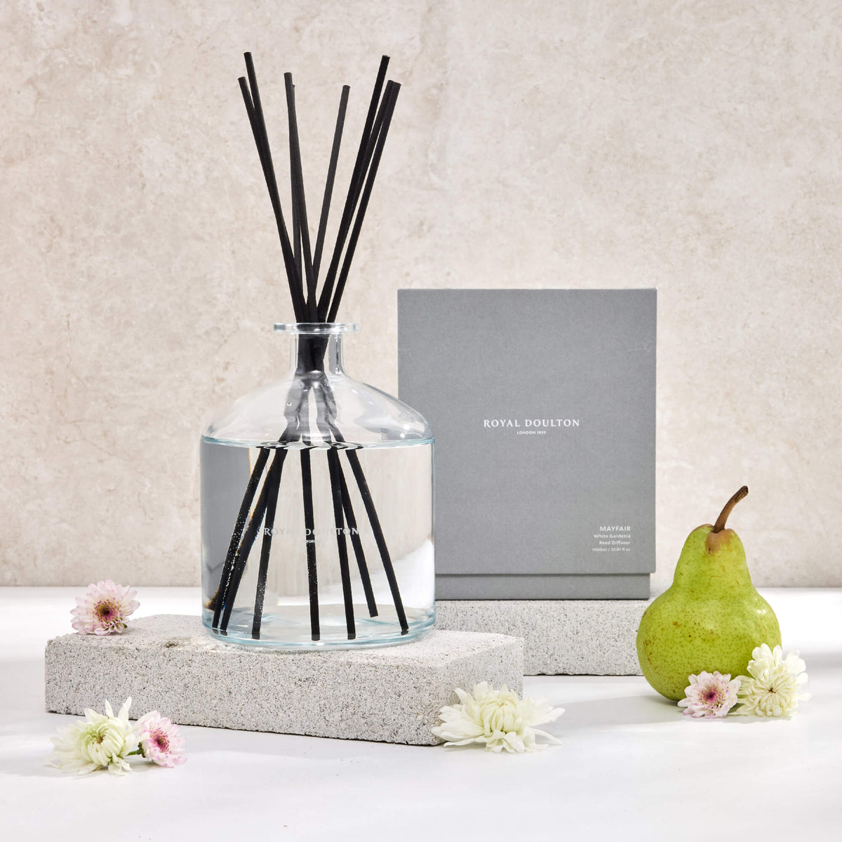 Royal Doulton Mayfair 1000ml diffuser and grey packaging box on pale blocks, with black reeds, a pear and flowers.
