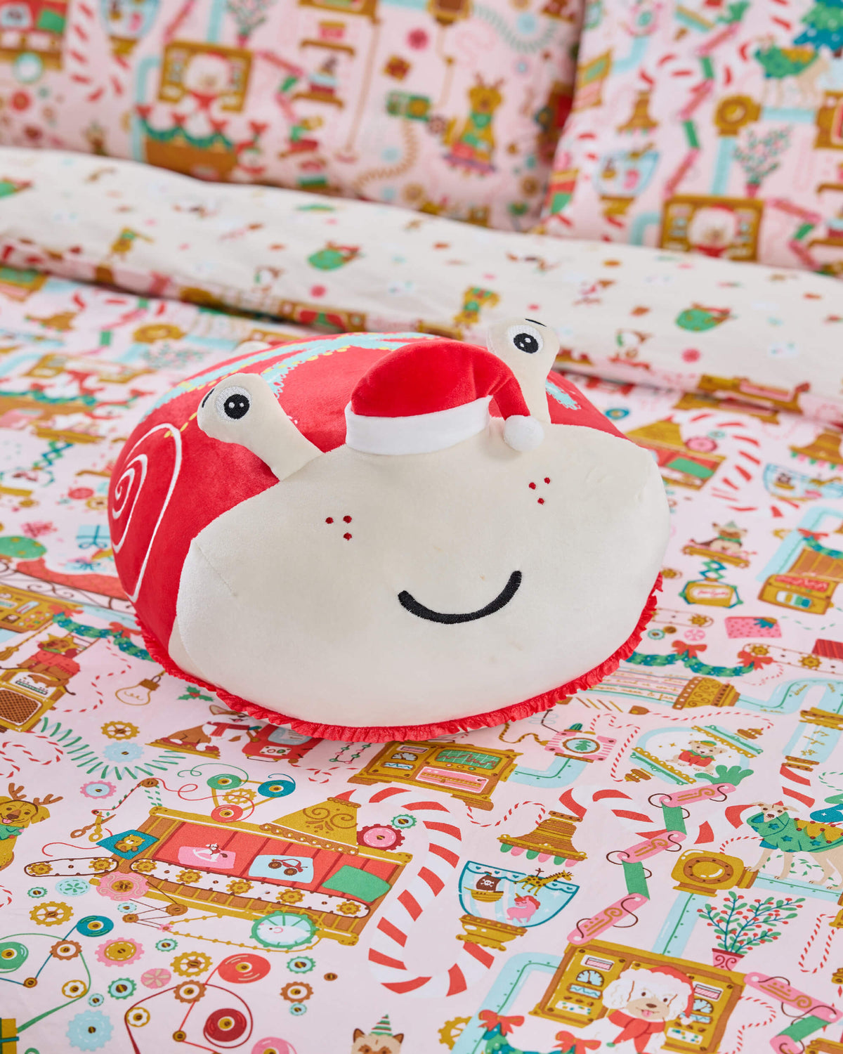 Red-and-cream Twill & Co snail cushion with a Santa hat resting on colourful festive bedding
