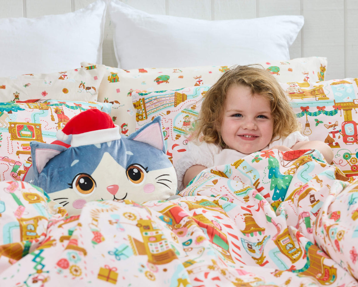 Child tucked into Twill & Co Woofshop bedding beside a round blue Christmas cat cushion