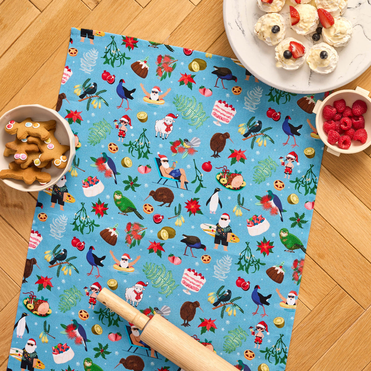 Blue Twill & Co Kiwiana Christmas tea towel with festive birds and New Zealand motifs beside baking treats
