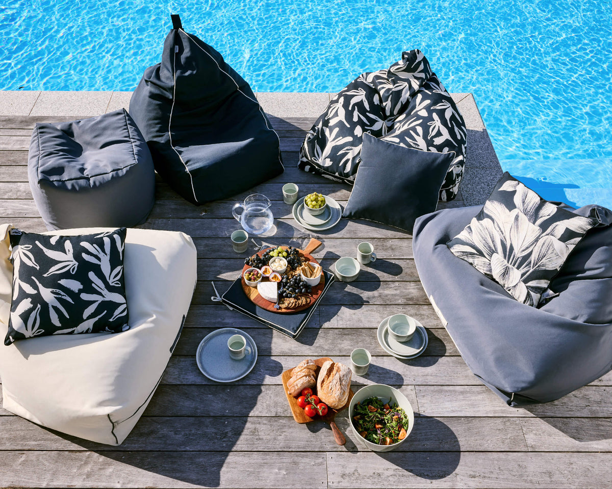 Overhead view of charcoal, cream and botanical-print Twill & Co seating around a picnic beside a blue pool
