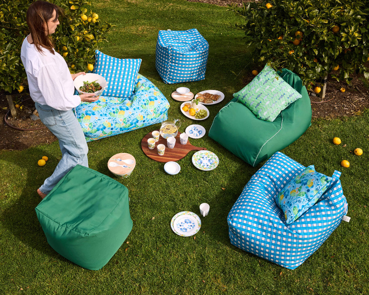 Person holding a bowl beside blue checked, lemon-print and green Twill & Co seating arranged on a lawn
