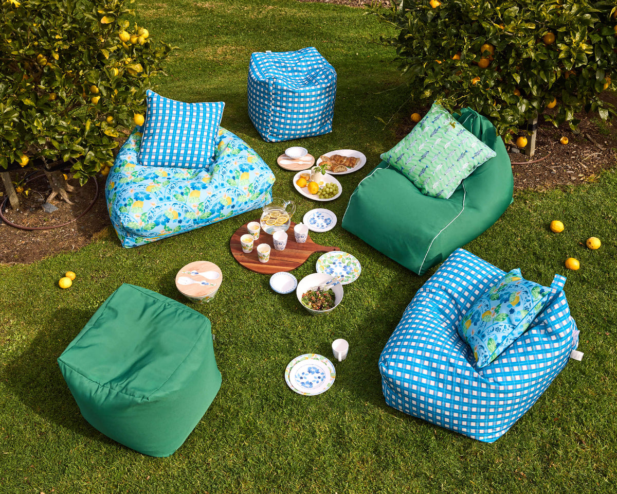 Overhead garden view of Twill & Co blue and green bean bags, cushions and picnic tableware among citrus trees