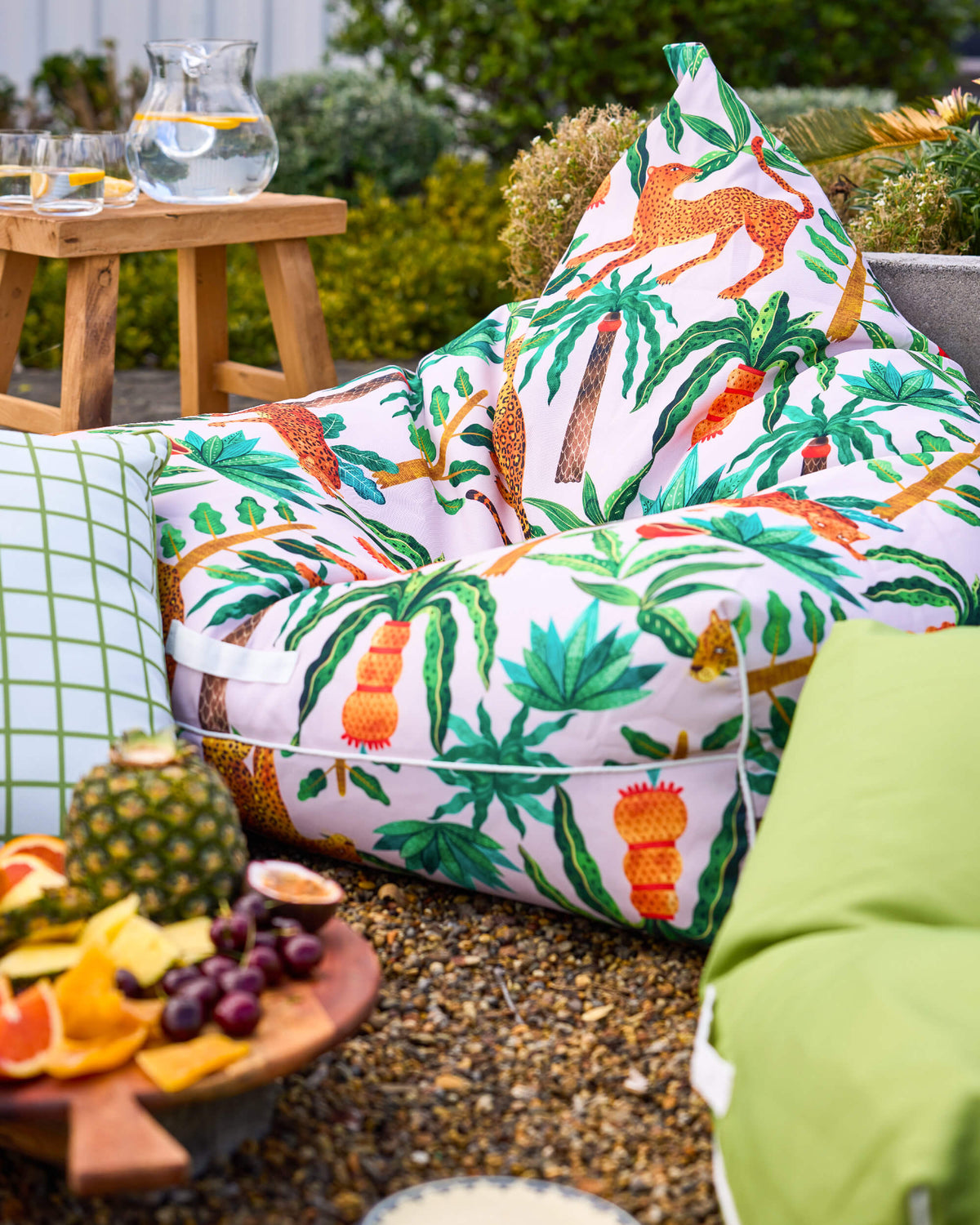 Twill & Co Tigerlily bean bag with orange leopards and tropical leaves beside a green checked cushion