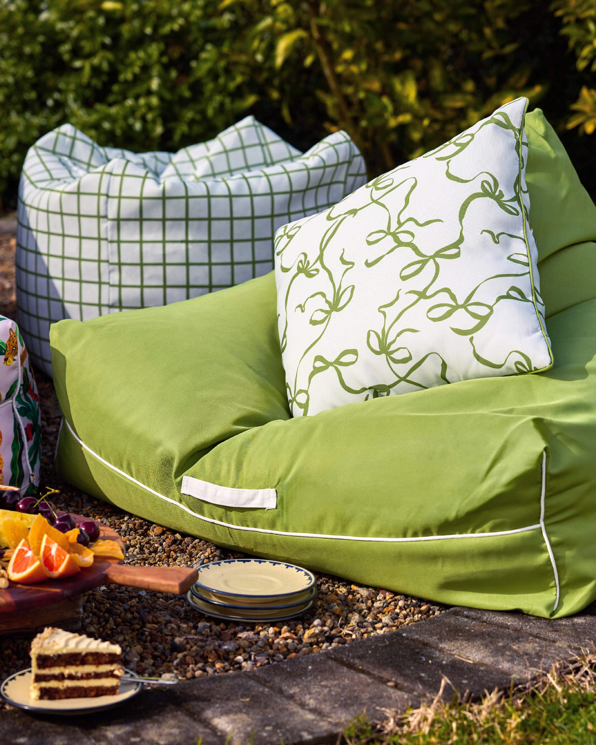 Lime-green Twill & Co bean bag with a bow-print cushion beside a checked ottoman and a garden picnic