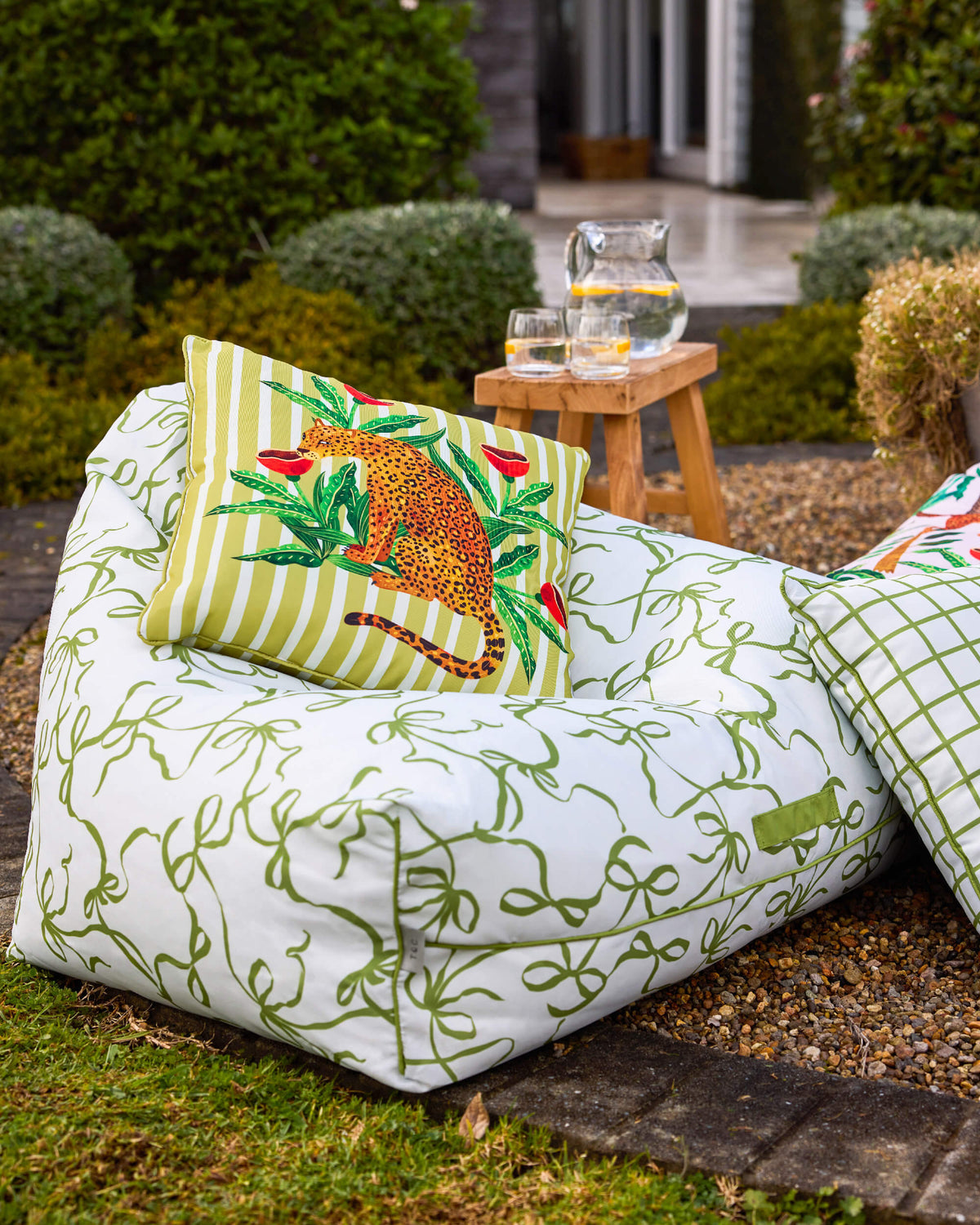 White Twill & Co bean bag with green ribbon bows and a striped leopard cushion in a garden