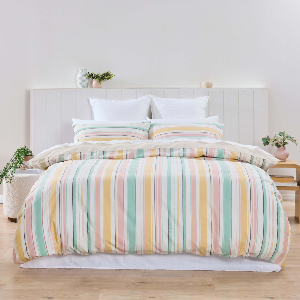 Front view of Twill & Co Dion striped bedding in pink, yellow, blue and green against a white headboard