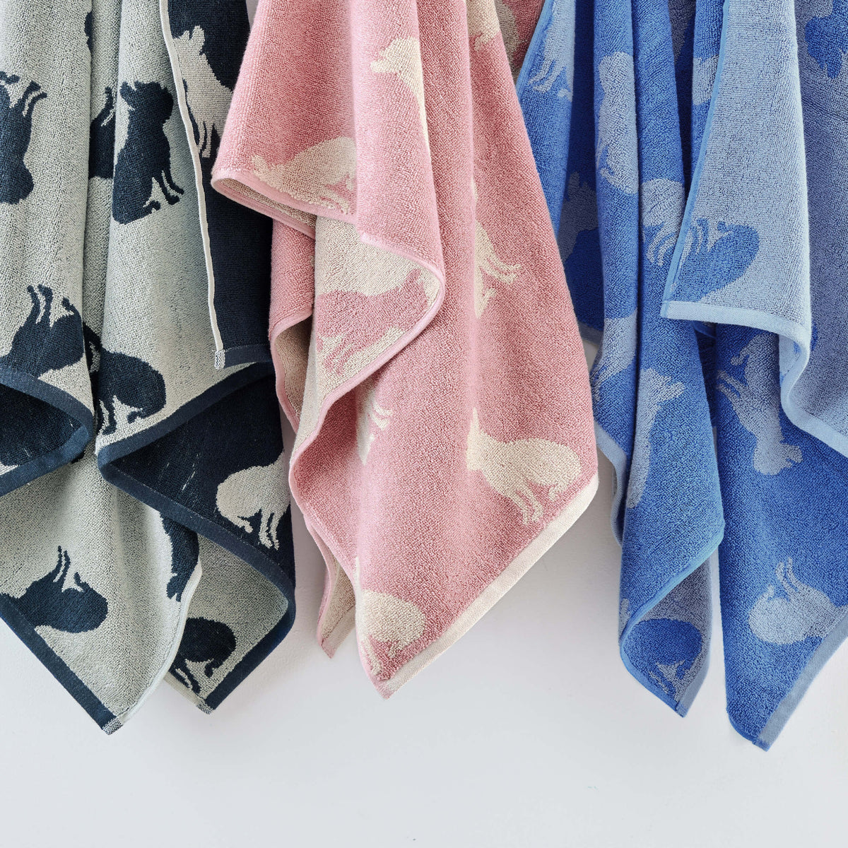 Twill & Co dog-patterned towels hanging side by side in charcoal, pink and blue