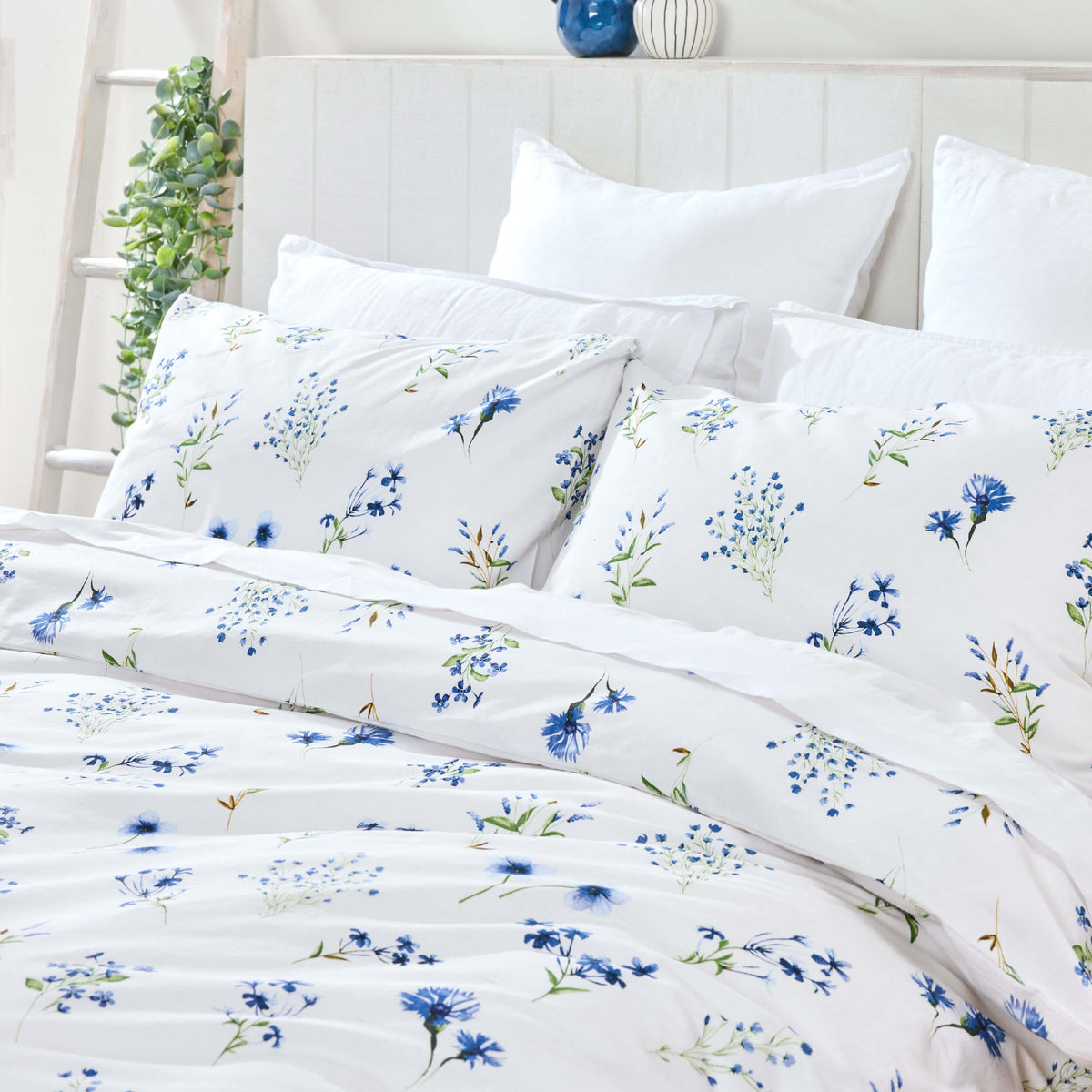 Twill & Co Belle bedding with small blue flowers and green stems on white beside a trailing houseplant