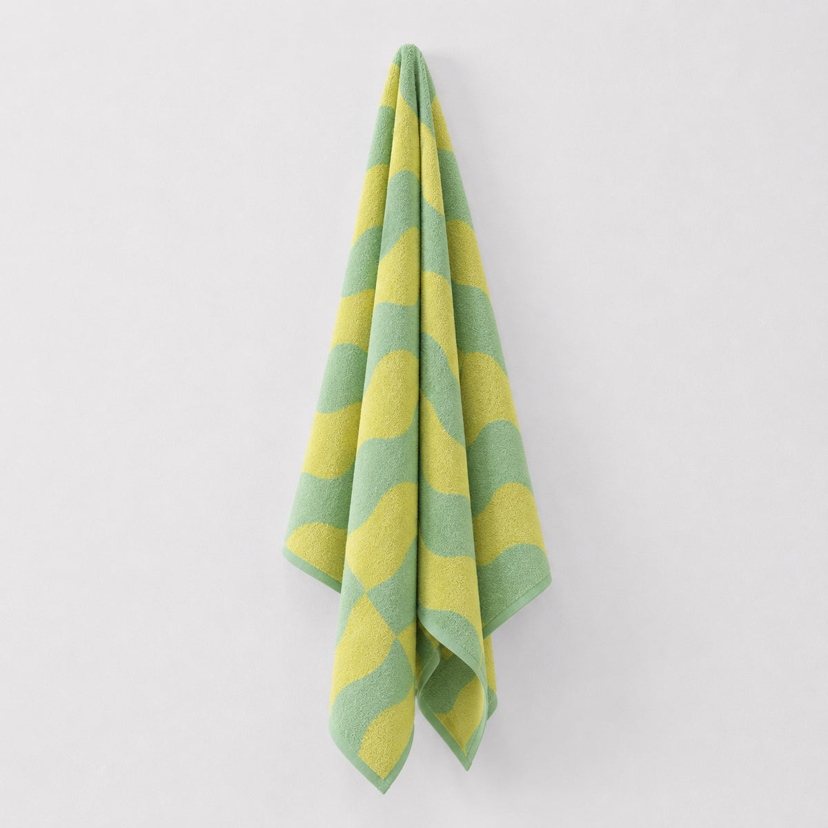 Twill & Co Squiggle Lemon Lime beach towel hanging against a pale wall