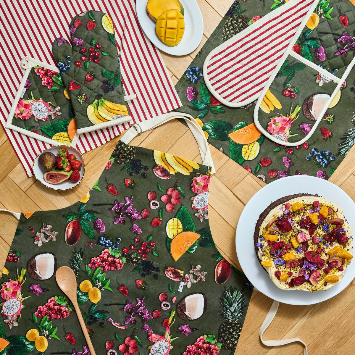 Twill & Co Exotic Fruits kitchen textiles with colourful fruit on dark green beside red-striped cloths