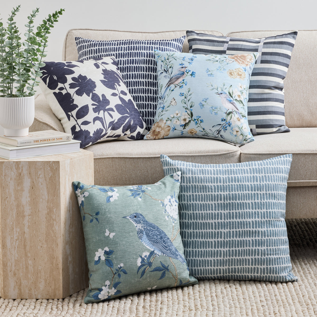 June & Jupiter blue floral, bird and striped cushions arranged on a sofa and rug