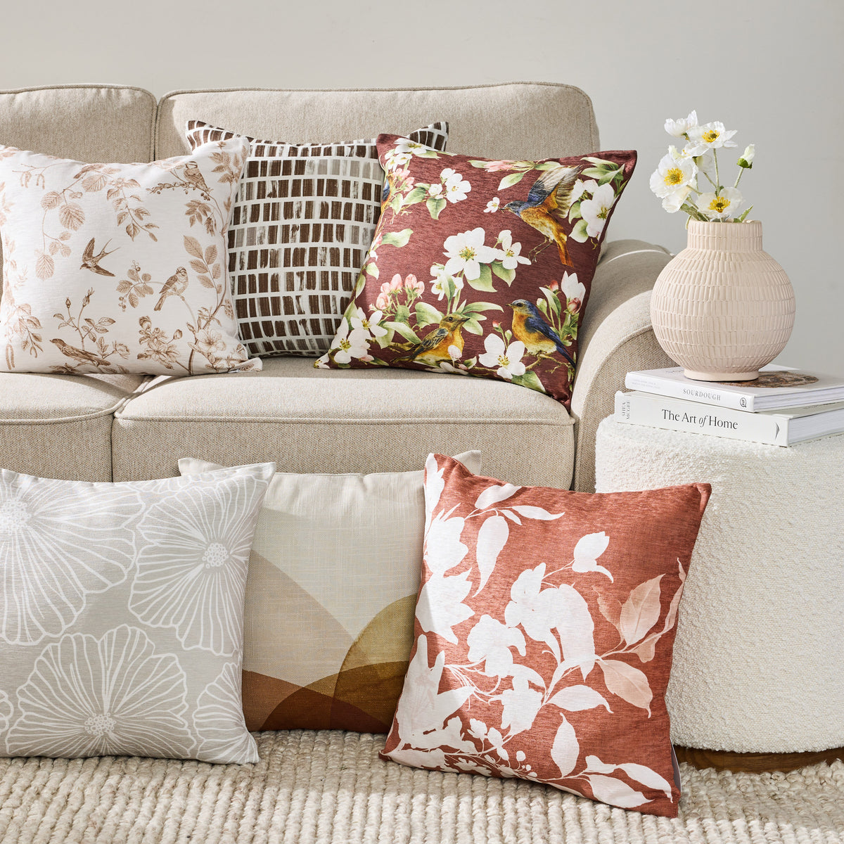June & Jupiter cushions in warm floral, geometric and leaf patterns arranged on and below a sofa