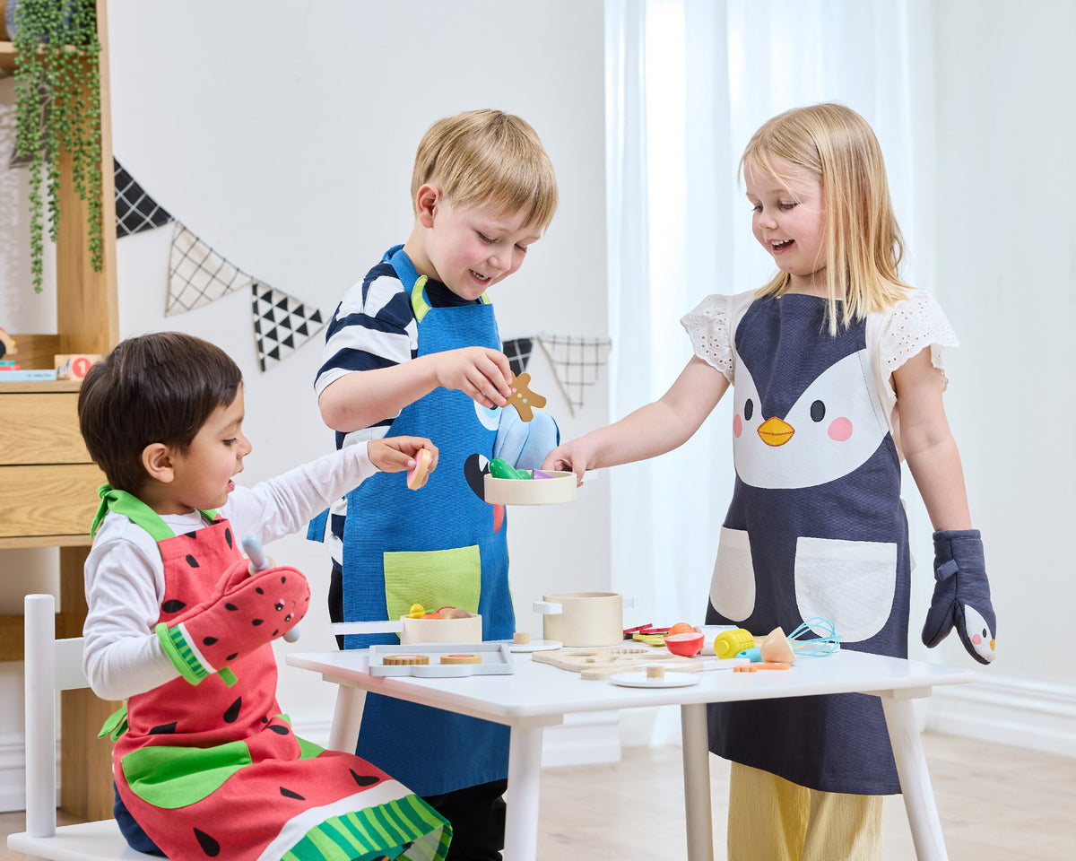 Children wearing colourful Twill & Co aprons while preparing pretend food around a small table