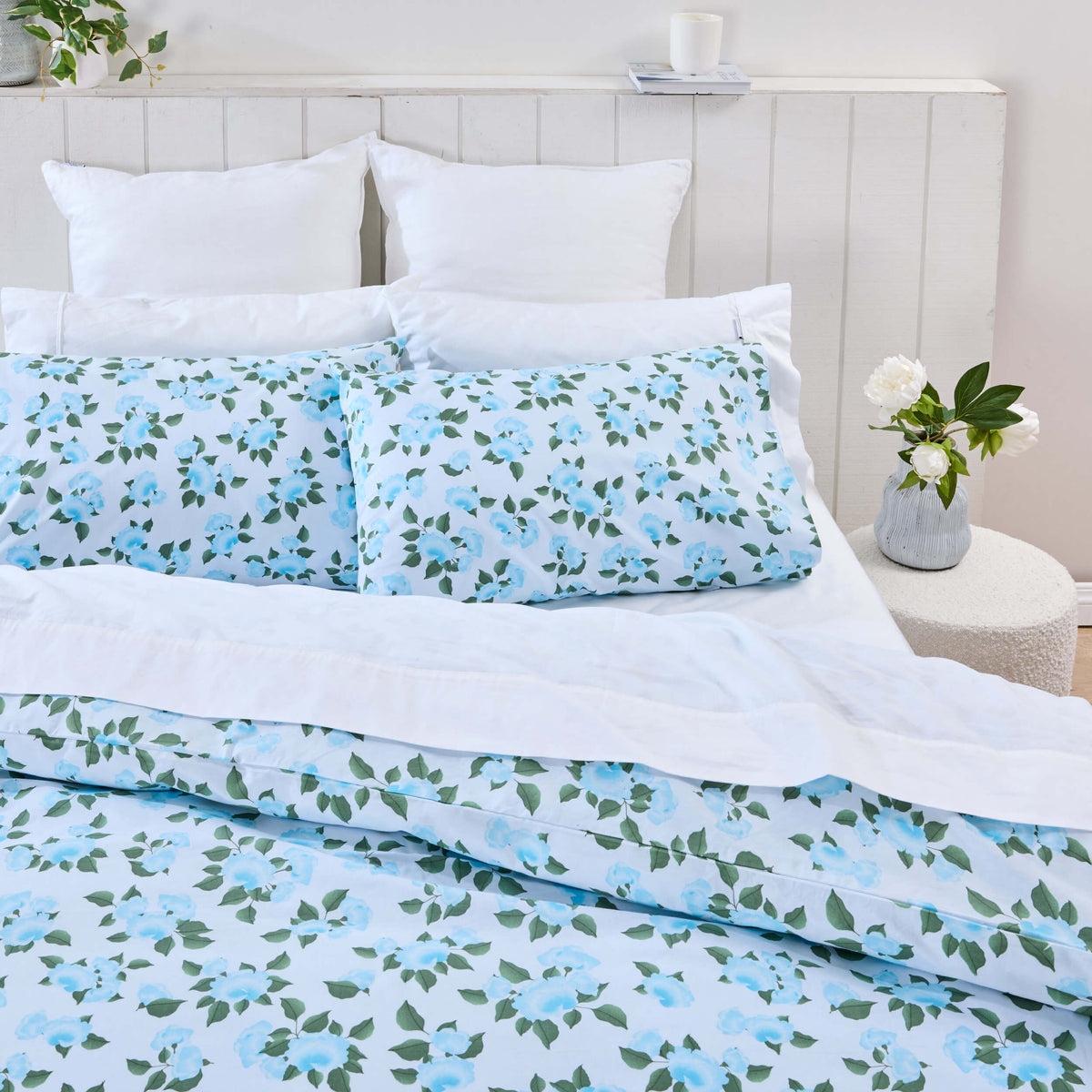 Twill & Co Marcy bedding with blue flowers and green leaves beneath a folded white sheet