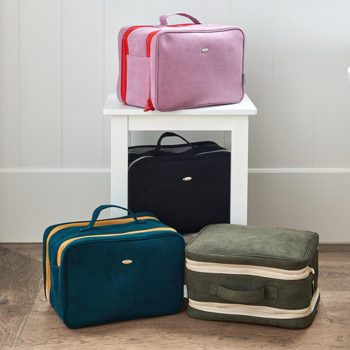 Pink, black, teal and olive zippered bags arranged on and around a white stool