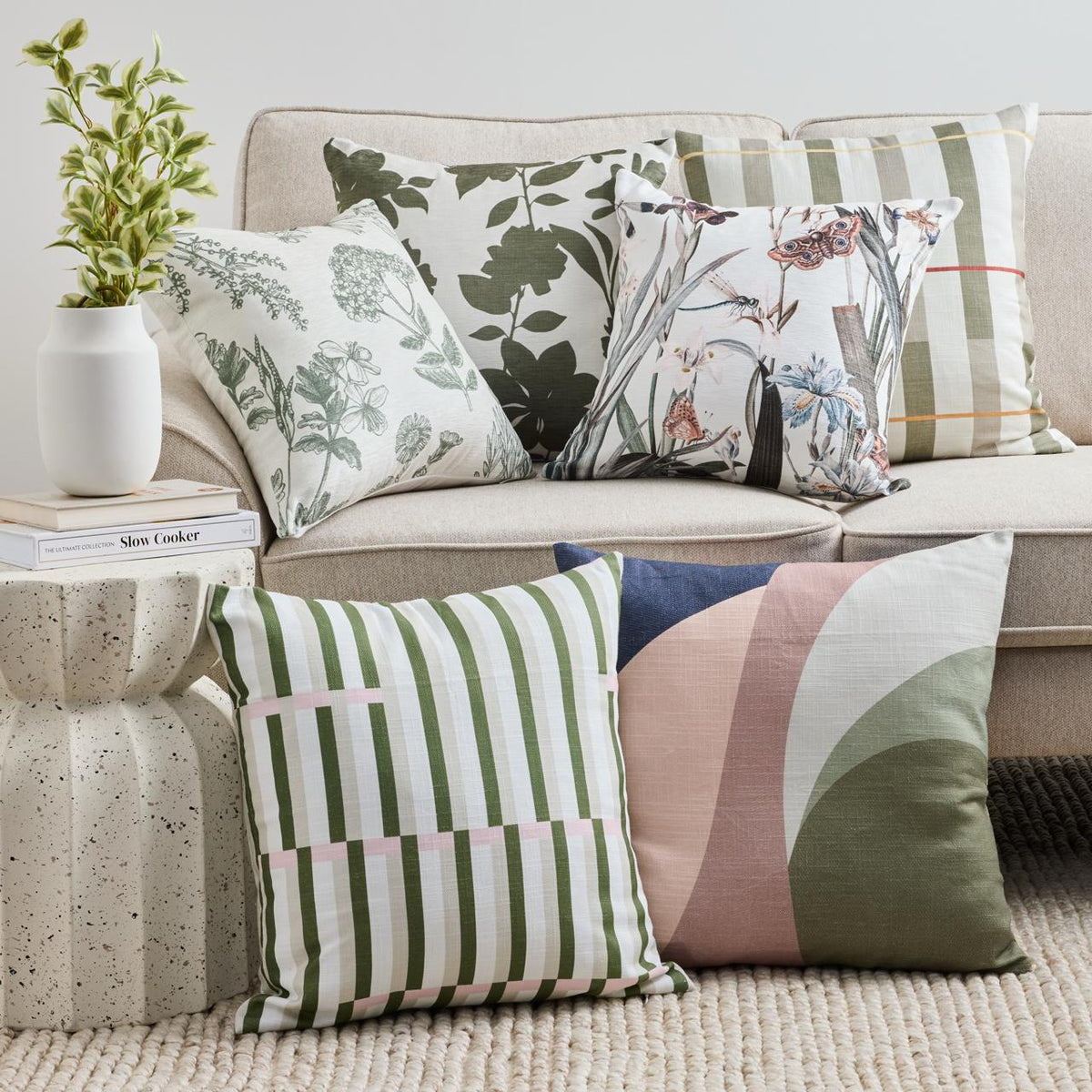 Botanical, checked and geometric cushions in green, pink and blue arranged on and beside a pale sofa